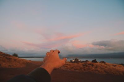 Cropped hand of man gesturing against sky during sunset