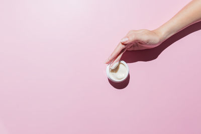 Woman hand with a cream on on a pink background. groomed hands, natural short nails