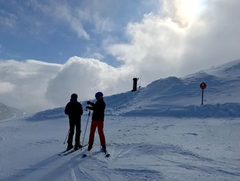 Rear view of people on snowcapped mountain against sky