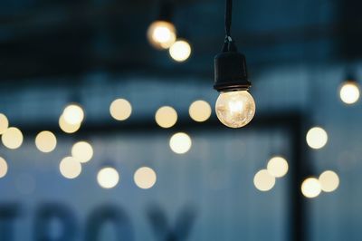 Close-up of illuminated light bulb hanging at night