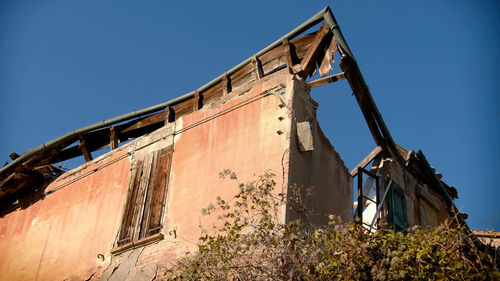 Low angle view of abandoned building against clear blue sky