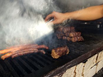 Cropped image of hand cooking sausages on barbeque