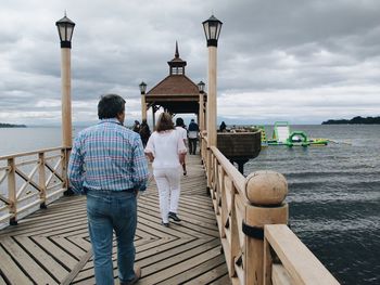 Rear view of people walking on pier against sea