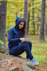 Portrait of young woman sitting on tree trunk in forest