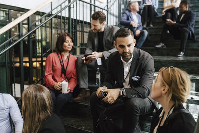 Businessman discussing with female professional while sitting on staircase during networking event