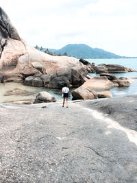 Rear view of woman standing on rock against sky