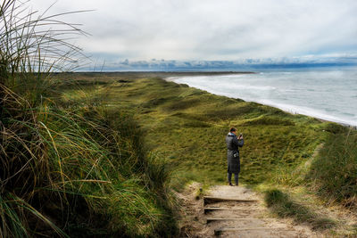 Rear view of man walking by sea against sky