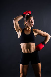 Portrait of young woman exercising against black background