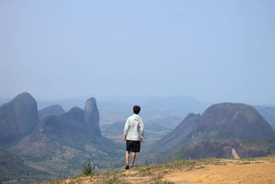 Rear view of man walking on mountain against clear sky