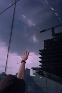 Low angle view of person hand by building against sky