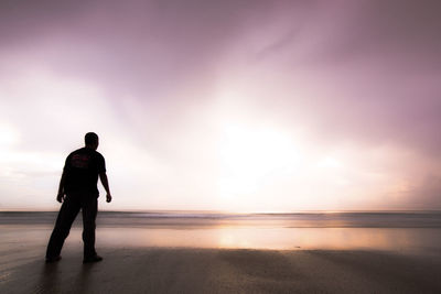 Silhouette man standing on beach against sky during sunset