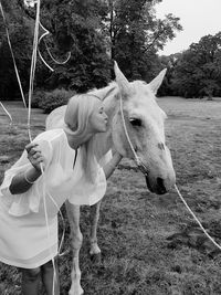 Woman kissing horse while standing on grassy field