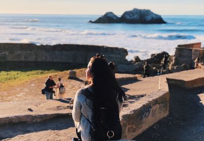 Rear view of woman relaxing on retaining wall against sea