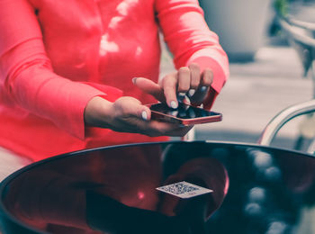 Hands of a young caucasian woman scan the menu on a glass table using a mobile phone