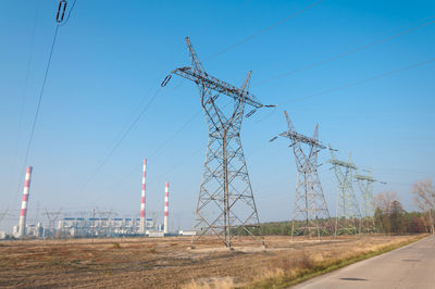 Electricity pylons on field against clear blue sky