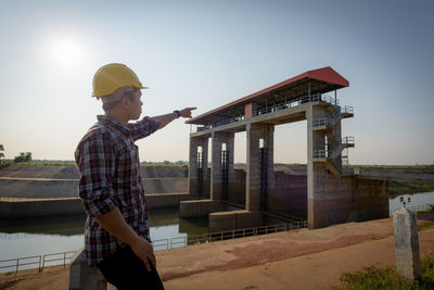 Manual worker pointing while standing at construction site against sky