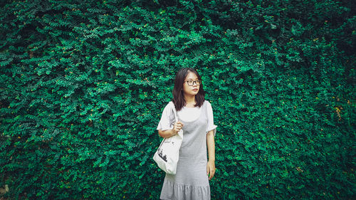 Young woman standing against plants