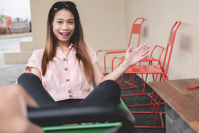 Portrait of young woman sitting in wheelbarrow against wall