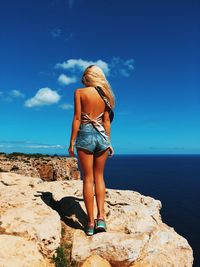 Rear view of young woman standing on rock against sea