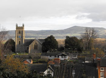 Houses and church by trees and buildings against sky