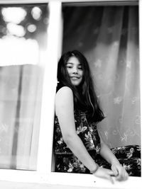 Portrait of young woman standing against window at home
