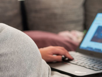 Midsection of woman using laptop while sitting on sofa at home