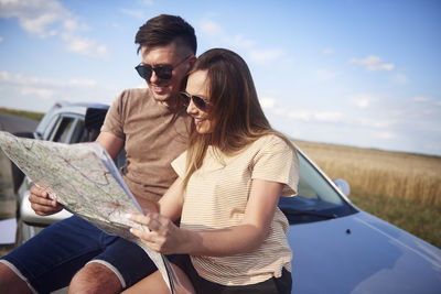 Couple reading map on car against sky