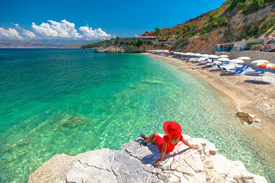 Rear view of woman sitting on rock by sea against sky