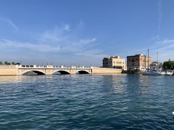 Bridge over river by buildings against blue sky