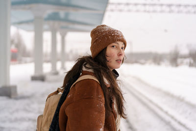 Young woman wait for train arrival at railway station outdoor during cold frosty snowy winter day