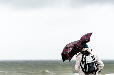 Rear view of woman with umbrella against sky