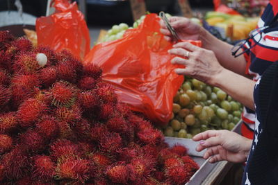 Midsection of women buying rambutan from market stall