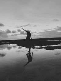 Silhouette man in lake against sky during sunset