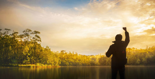 Silhouette man standing by lake against sky during sunset