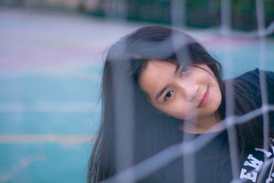 Portrait of young woman on court seen through net