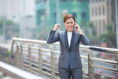 Angry businesswoman talking on mobile phone on bridge in city