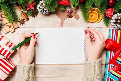 Top view of hand writing in a notebook on christmas background. fir tree and festive decorations.