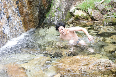 High angle view of shirtless young man screaming while crouching in river