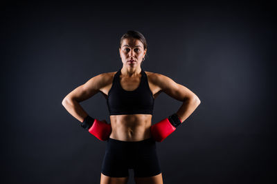 Portrait of young woman standing against black background