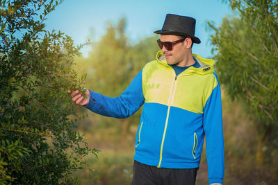 Young man wearing sunglasses standing against plants