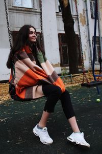 Teenage girl sitting on swing against old building