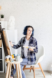 Young woman sitting on table against wall