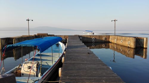 Sailboats moored on pier by sea against clear blue sky