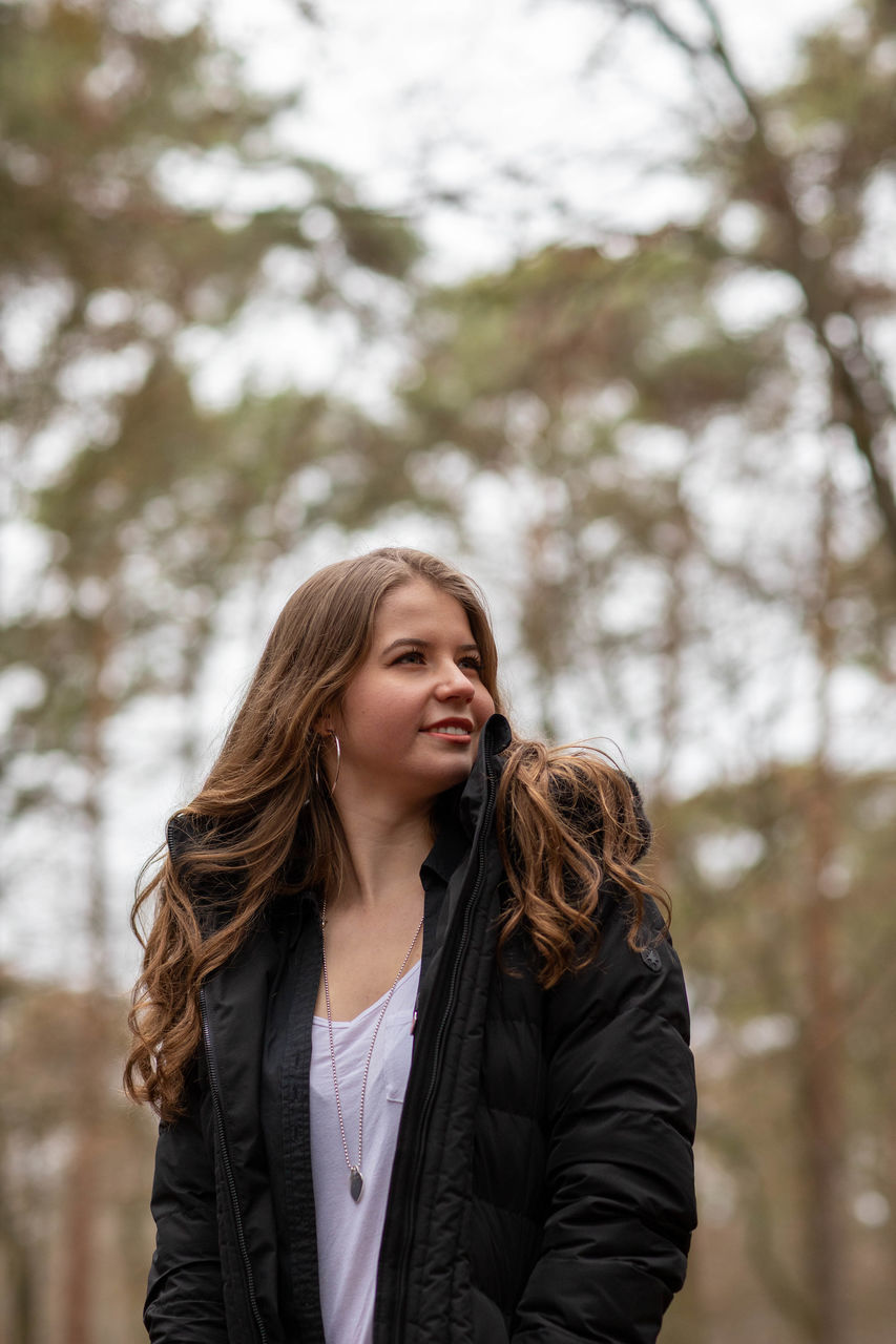 one person, focus on foreground, tree, young adult, young women, clothing, lifestyles, jacket, long hair, hair, front view, leisure activity, waist up, winter, warm clothing, hairstyle, standing, women, beauty, beautiful woman, outdoors, scarf, leather, teenager