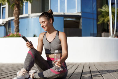 Young woman using smart phone while sitting outdoors