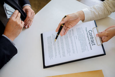 Cropped hands of man giving contract papers for signing to businessman