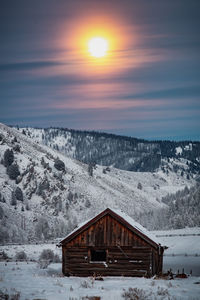 House on snowcapped mountain against sky during sunset