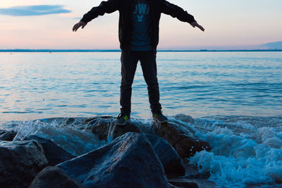 Low section of man with arms outstretched
standing at sea shore