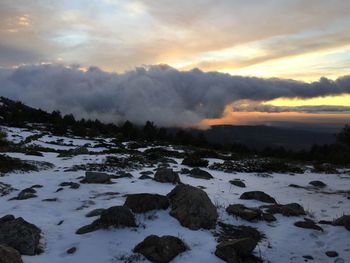 Snow covered landscape against sky during sunset