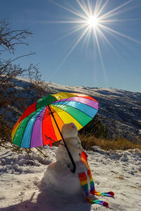 Snowman with umbrella in lgtb pride colors on a background of snowymountains with starry sun and sky